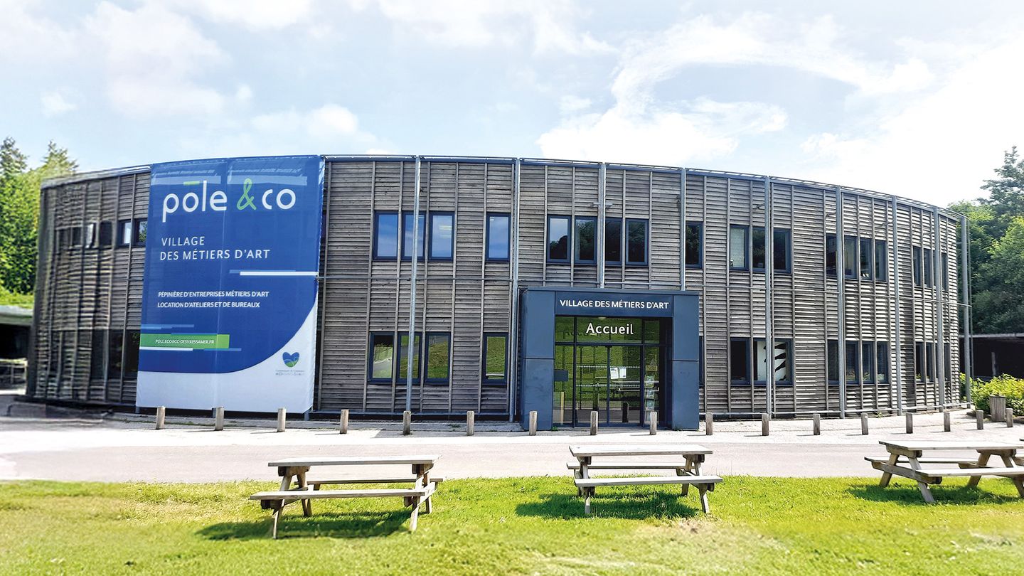 Façade courbe en bois du Village des métiers d'art de Desvres, avec l'entrée et les tables de pique-nique sur la pelouse